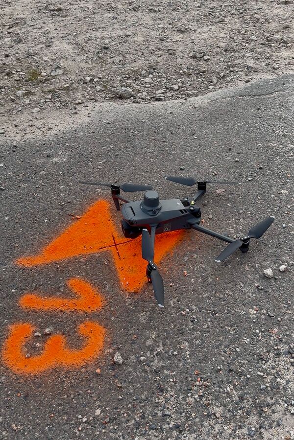 Startbereite DJI-Drohne mit Kamera und RTK-Modul steht neben einem nummerierten, orange markierten Passpunkt auf Asphalt